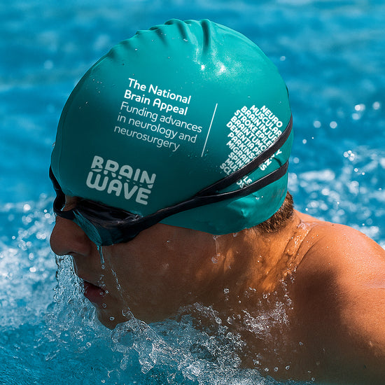 Swimmer wearing The National Brain Appeal Brain Wave teal swim cap in a pool, promoting neurological charity fundraising and awareness.